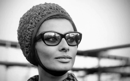 Black and white HD desktop wallpaper of celebrity Sophia Loren wearing a textured headscarf and large dark sunglasses, gazing thoughtfully into the distance.