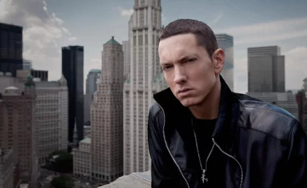HD desktop wallpaper featuring Eminem in front of a cityscape with towering buildings and a cloudy sky. The image has a musical theme.