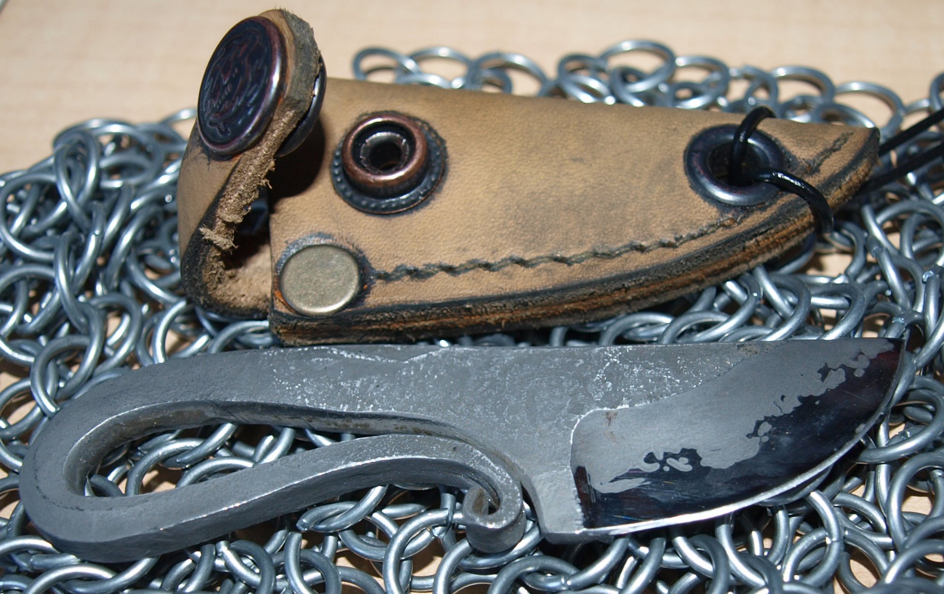 A high-definition desktop wallpaper featuring a handmade knife and its leather sheath, set against a backdrop of interlocking metal chains, emphasizing craftsmanship and detail.