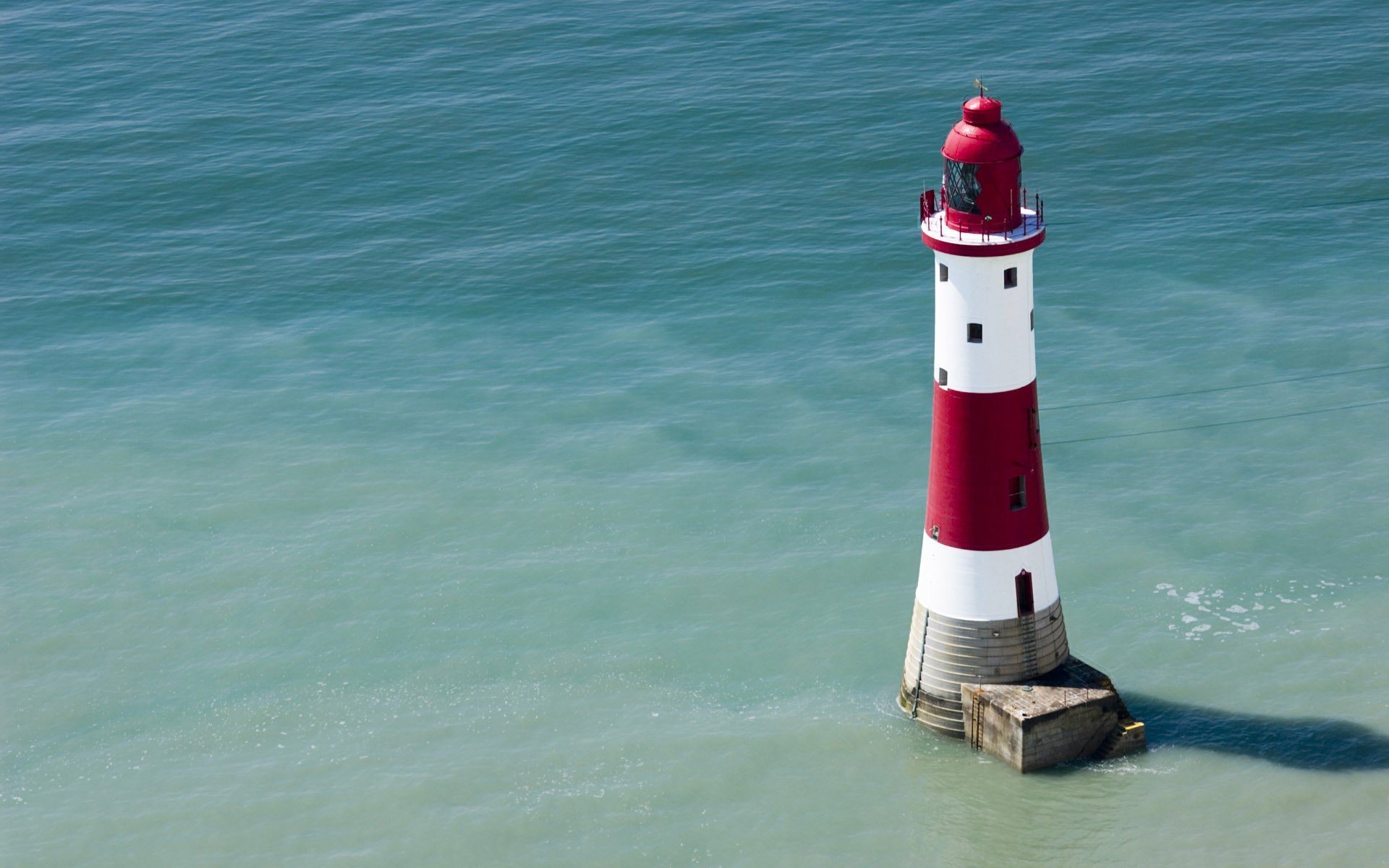 HD desktop wallpaper featuring a man-made lighthouse with red and white stripes standing in calm blue-green water.