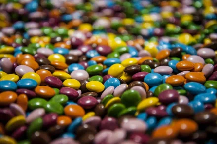 A vibrant HD desktop wallpaper featuring an array of colorful chocolate candies scattered across the image.