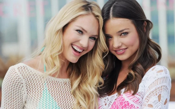 Candice Swanepoel and Miranda Kerr smile together in a vibrant outdoor setting, showcasing their friendship and charm in this HD desktop wallpaper.