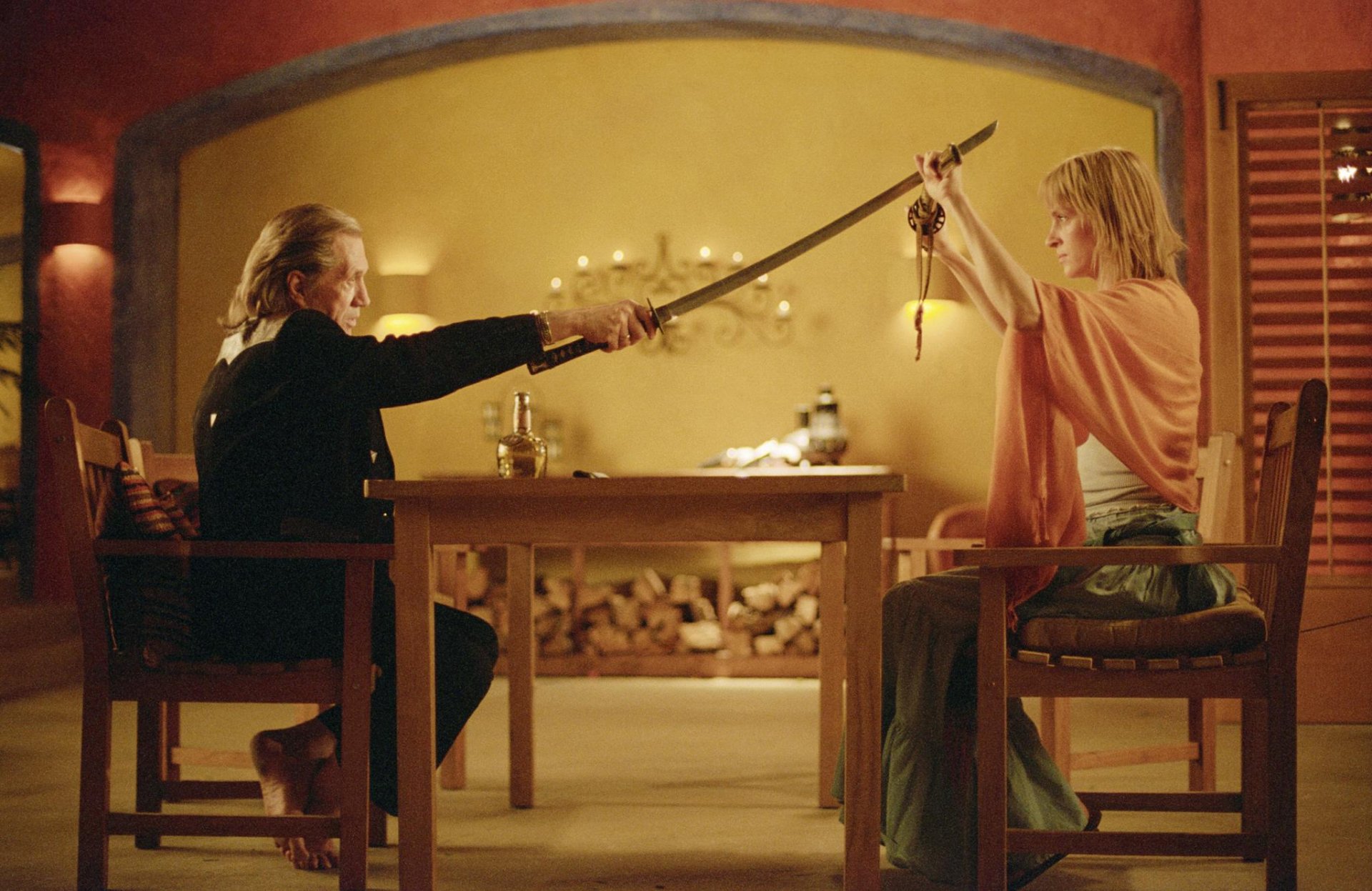 HD desktop wallpaper of a scene from Kill Bill: Vol. 2, featuring two characters in a tense sword standoff across a table.