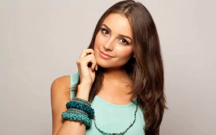 HD PC desktop wallpaper featuring celebrity Olivia Culpo with long brown hair, wearing a light blue top and turquoise bracelets against a neutral background.