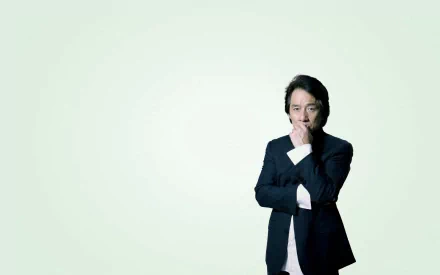 HD wallpaper of celebrity Jackie Chan in a thoughtful pose against a light green background.