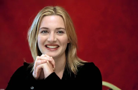 HD wallpaper featuring celebrity Kate Winslet sitting against a vibrant red background, smiling warmly with hands clasped.