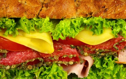 HD PC desktop wallpaper featuring a close-up of a fresh sandwich with lettuce, cheese, tomato, salami, and ham on crusty bread.