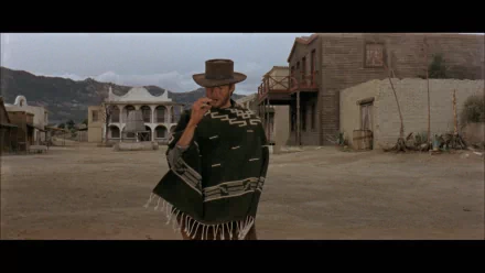 HD PC desktop wallpaper background from the movie A Fistful of Dollars: lone gunslinger in a poncho and wide-brimmed hat strides into a dusty frontier town, wide cinematic framing.