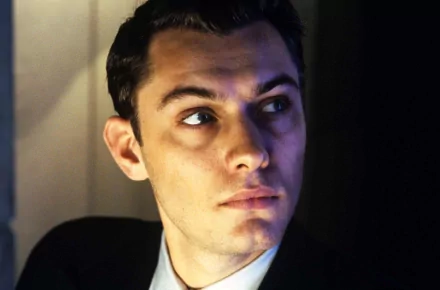 HD desktop wallpaper featuring a still from Gattaca with a focused man in suit looking upwards, posed against a dark background.