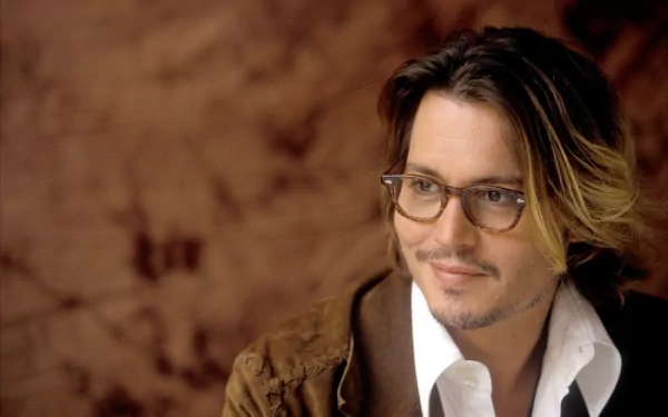 HD PC desktop wallpaper featuring celebrity Johnny Depp with a thoughtful expression, wearing glasses and a brown jacket against a warm brown background.