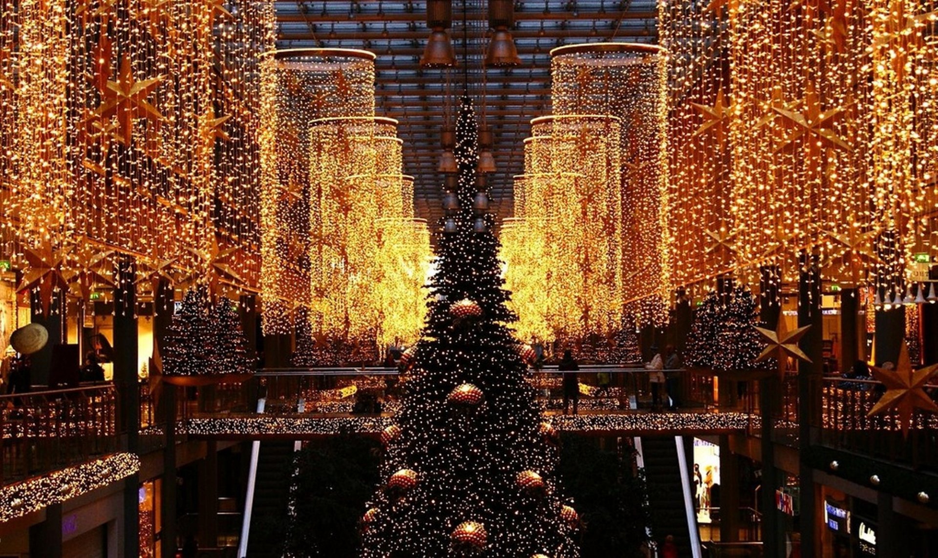 HD PC desktop wallpaper featuring a grand indoor Christmas tree surrounded by cascading golden holiday lights creating a festive and warm atmosphere.