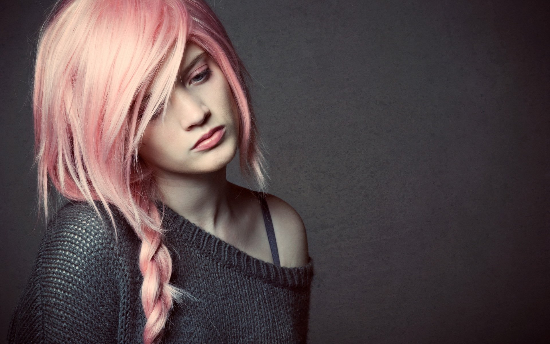 A woman with pink hair and a braid gazes thoughtfully, wearing a cozy sweater against a dark backdrop, creating a moody atmosphere for a HD PC desktop wallpaper.