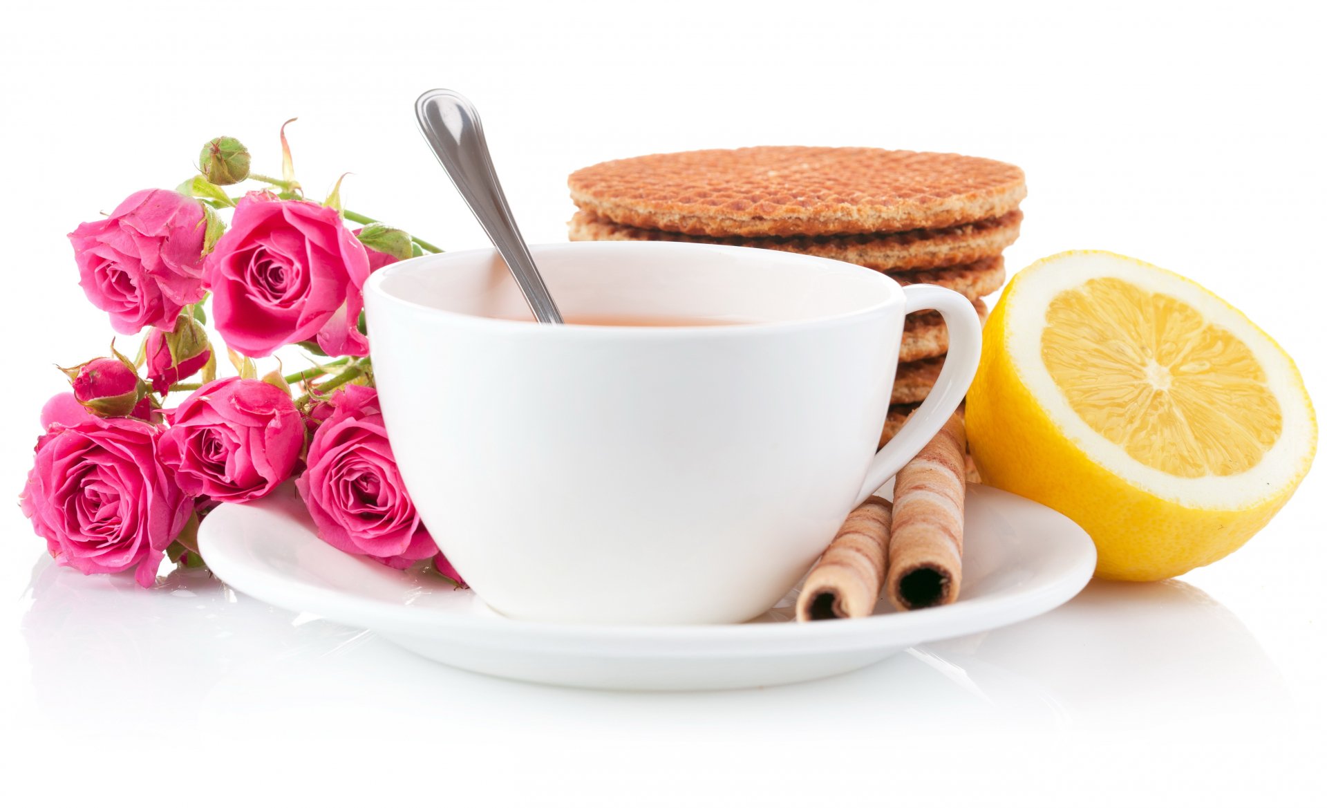 A 4K Ultra HD desktop wallpaper featuring a white cup of tea with a spoon, stacked cookies, a halved lemon, wafer rolls, and a small bouquet of pink roses on a white background.