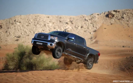 HD PC desktop wallpaper and background: Toyota vehicle — pickup truck airborne over desert dunes, kicking up sand beneath a clear blue sky.