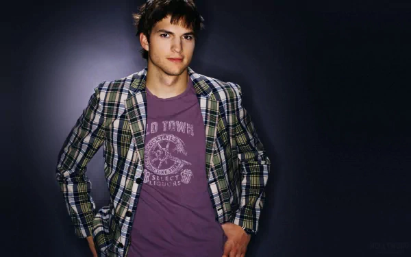 HD PC desktop wallpaper: young male celebrity in a plaid shirt and purple T‑shirt, hands in pockets, posed against a dark gradient background.