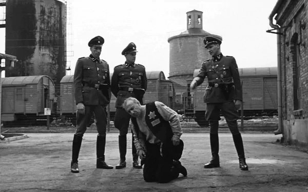 Black-and-white HD PC desktop wallpaper from the movie Schindler's List: a kneeling man in a train yard surrounded by three uniformed Nazi officers.