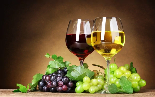HD desktop wallpaper featuring two wine glasses—one with red wine and one with white—surrounded by fresh green and purple grapes and green leaves against a warm background.