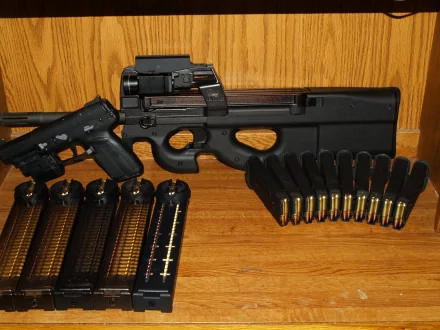 A high-definition desktop wallpaper featuring a FN P90 alongside a semi-automatic pistol and several magazines, set against a wooden background.