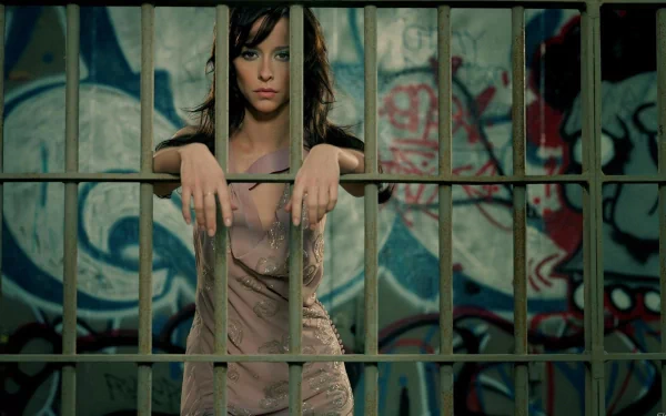 Jennifer Love Hewitt poses dramatically behind bars against a colorful, graffiti-covered background, creating an intriguing and artistic HD wallpaper for desktop use.