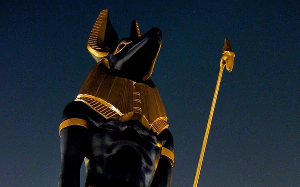 Artistic HD PC desktop wallpaper featuring a detailed Egyptian figure with a jackal head, adorned in traditional gold and black attire against a dark background.