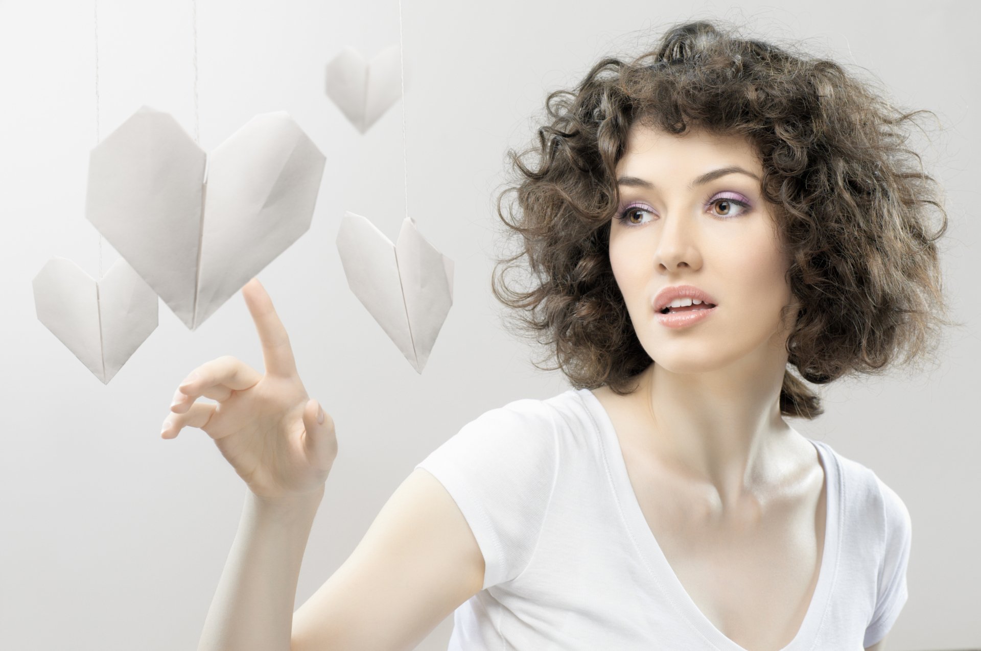 A beautiful woman with curly hair gently touches floating paper hearts in this 4K Ultra HD desktop wallpaper, showcasing a blend of elegance and creativity.