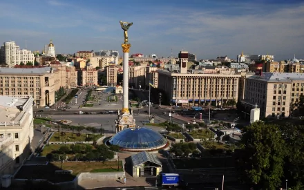 A vibrant street scene in Kiev, Ukraine, capturing city buildings, people, and the iconic Independence Monument under a clear sky, shown as an HD desktop wallpaper.