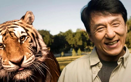 HD desktop wallpaper featuring Jackie Chan smiling next to a tiger in a natural outdoor setting.