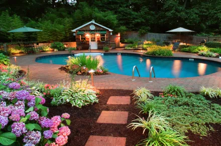 HD desktop wallpaper of a man-made, illuminated pool surrounded by lush garden plants, flowers, and seating areas in a serene outdoor setting.
