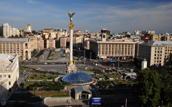 A vibrant street scene in Kiev, Ukraine, capturing city buildings, people, and the iconic Independence Monument under a clear sky, shown as an HD desktop wallpaper.