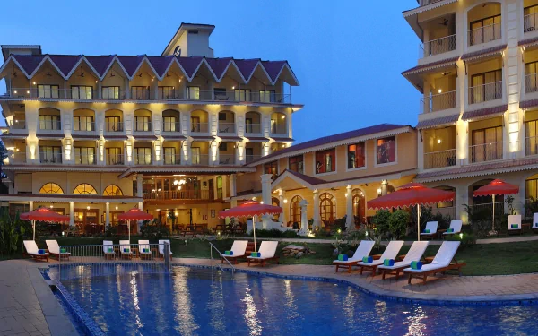 2K Quad HD PC desktop wallpaper: illuminated man-made resort with poolside loungers, red umbrellas, and multi-story hotel reflected in evening water.