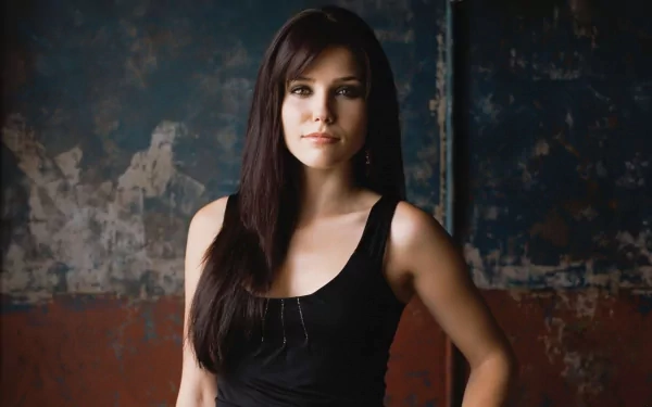 HD PC desktop wallpaper featuring a celebrity actress with long dark hair in a black tank top, standing confidently against a worn, textured industrial wall.