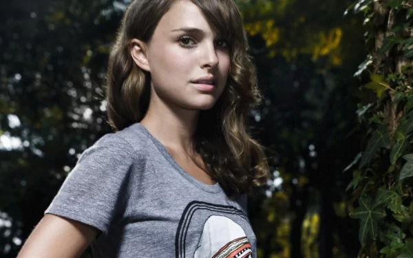 A striking HD wallpaper featuring Natalie Portman, showcasing her in a gray t-shirt, surrounded by lush greenery, capturing a blend of natural beauty and celebrity charm.