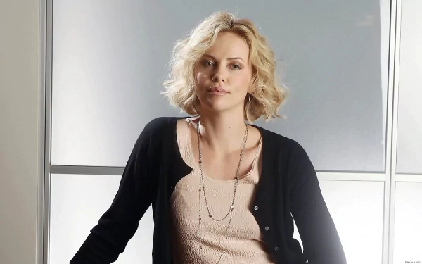 A high-definition desktop wallpaper featuring Charlize Theron, showcasing her with wavy blonde hair and a confident expression against a softly lit background.