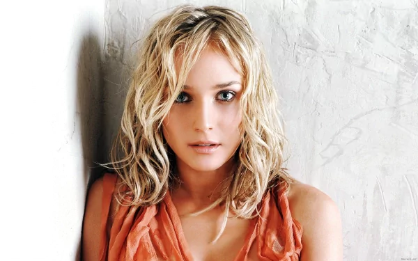Diane Kruger gazes directly at the camera with tousled blonde hair, against a textured light background. This HD wallpaper captures her striking beauty and allure.