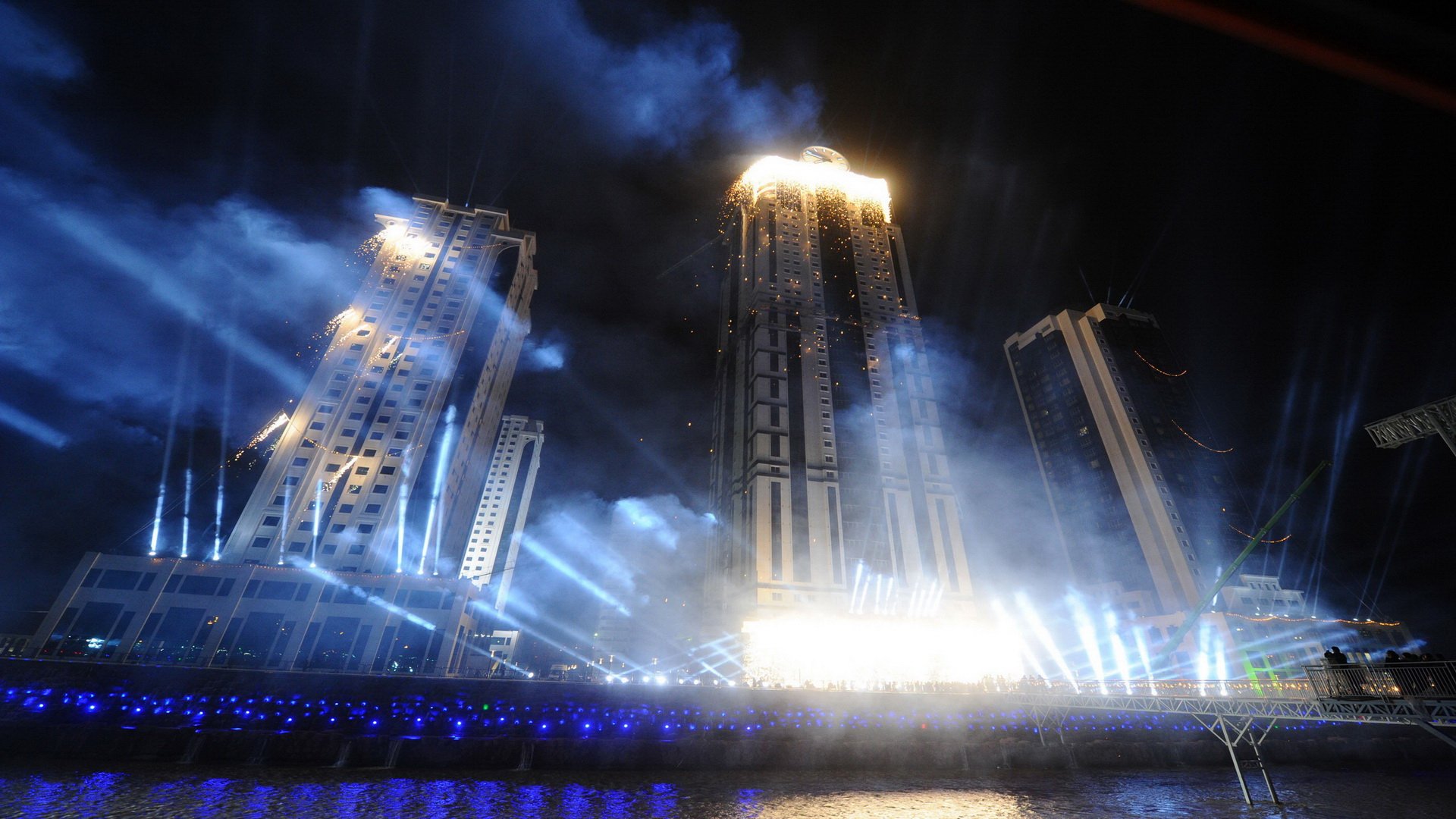 HD PC desktop wallpaper/background: illuminated man-made skyscrapers at night, beams of light and foggy reflections on the water creating a dramatic urban skyline.