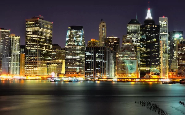 HD PC desktop wallpaper showing the vibrant nighttime skyline of Manhattan, New York, with illuminated city buildings reflecting over the water.