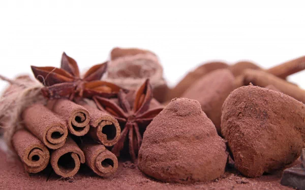 An enticing arrangement of chocolate truffles, cocoa powder, cinnamon sticks, and star anise captures the richness of food, presented in a vibrant 4K Ultra HD desktop wallpaper.