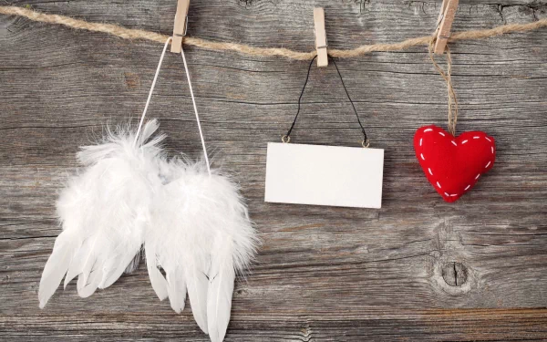 4K Ultra HD Valentine's Day desktop wallpaper featuring white angel wings, a blank hanging sign, and a red stitched heart hanging on a rustic wooden background.