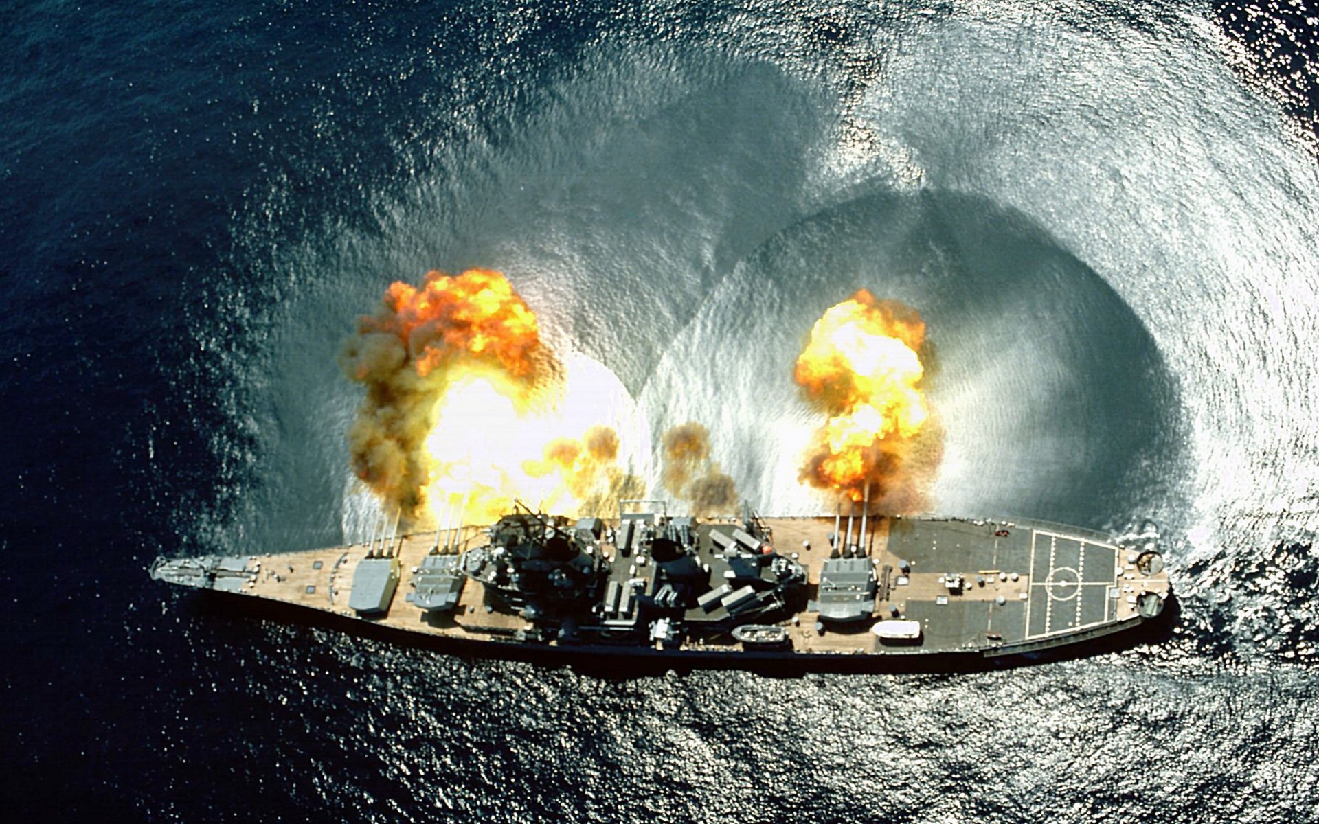 A dramatic HD wallpaper of USS Iowa (BB-61) in action, showcasing explosions and military might against a vibrant ocean backdrop.