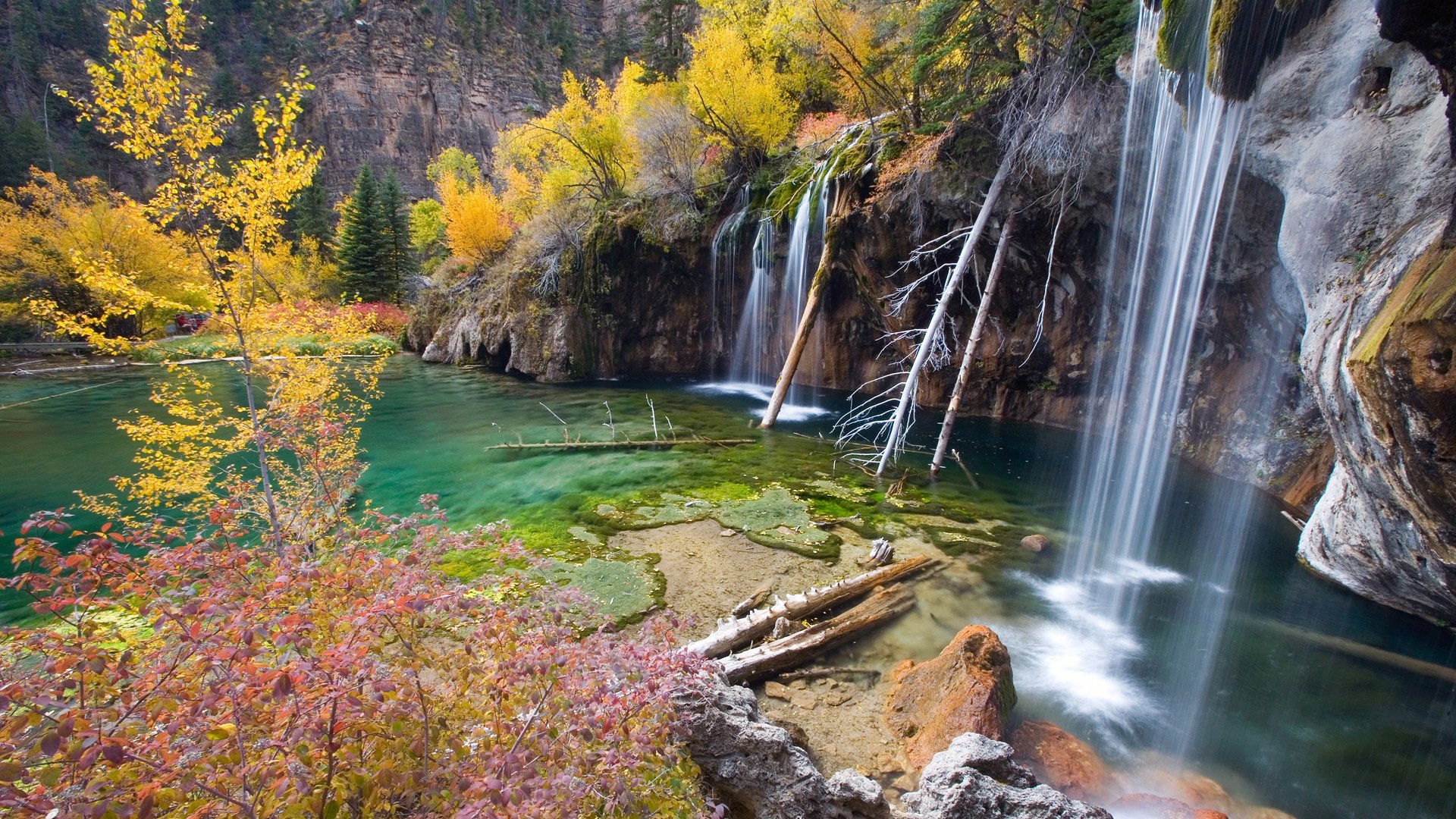 HD desktop wallpaper of Hanging Lake featuring clear turquoise water, vibrant autumn trees, and cascading waterfalls surrounded by natural rock formations.
