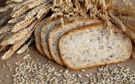 HD PC desktop wallpaper showing sliced whole grain bread surrounded by wheat stalks and scattered grains, highlighting natural, wholesome food elements.