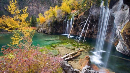 HD desktop wallpaper of Hanging Lake featuring clear turquoise water, vibrant autumn trees, and cascading waterfalls surrounded by natural rock formations.