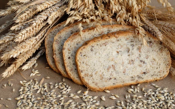 HD PC desktop wallpaper showing sliced whole grain bread surrounded by wheat stalks and scattered grains, highlighting natural, wholesome food elements.