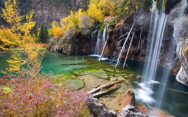 HD desktop wallpaper of Hanging Lake featuring clear turquoise water, vibrant autumn trees, and cascading waterfalls surrounded by natural rock formations.