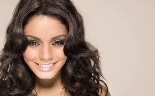 Close-up HD desktop wallpaper of celebrity Vanessa Hudgens smiling with wavy dark hair against a plain beige background.