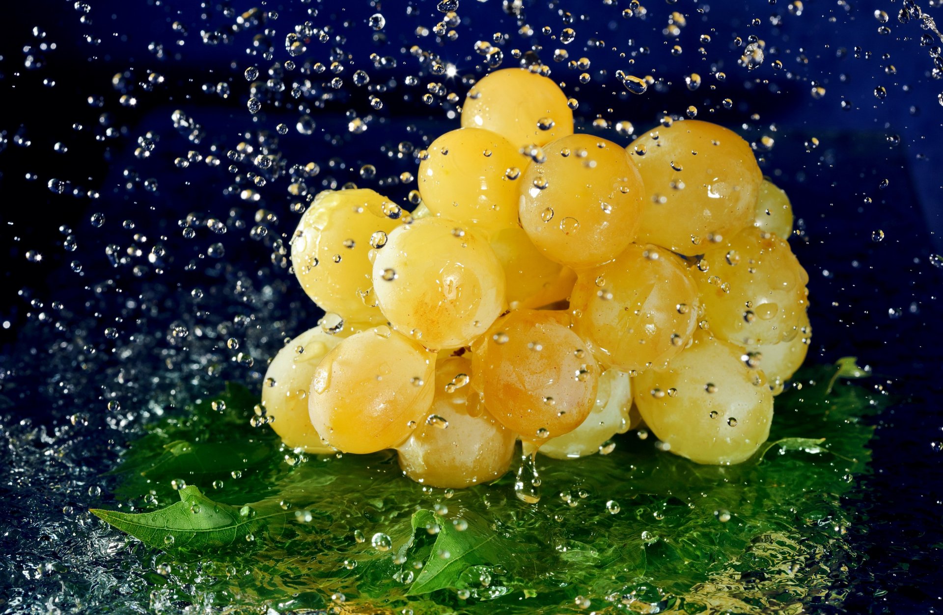 A cluster of yellow grapes with water droplets splashing around, captured in vibrant detail as a 4K Ultra HD food desktop wallpaper.