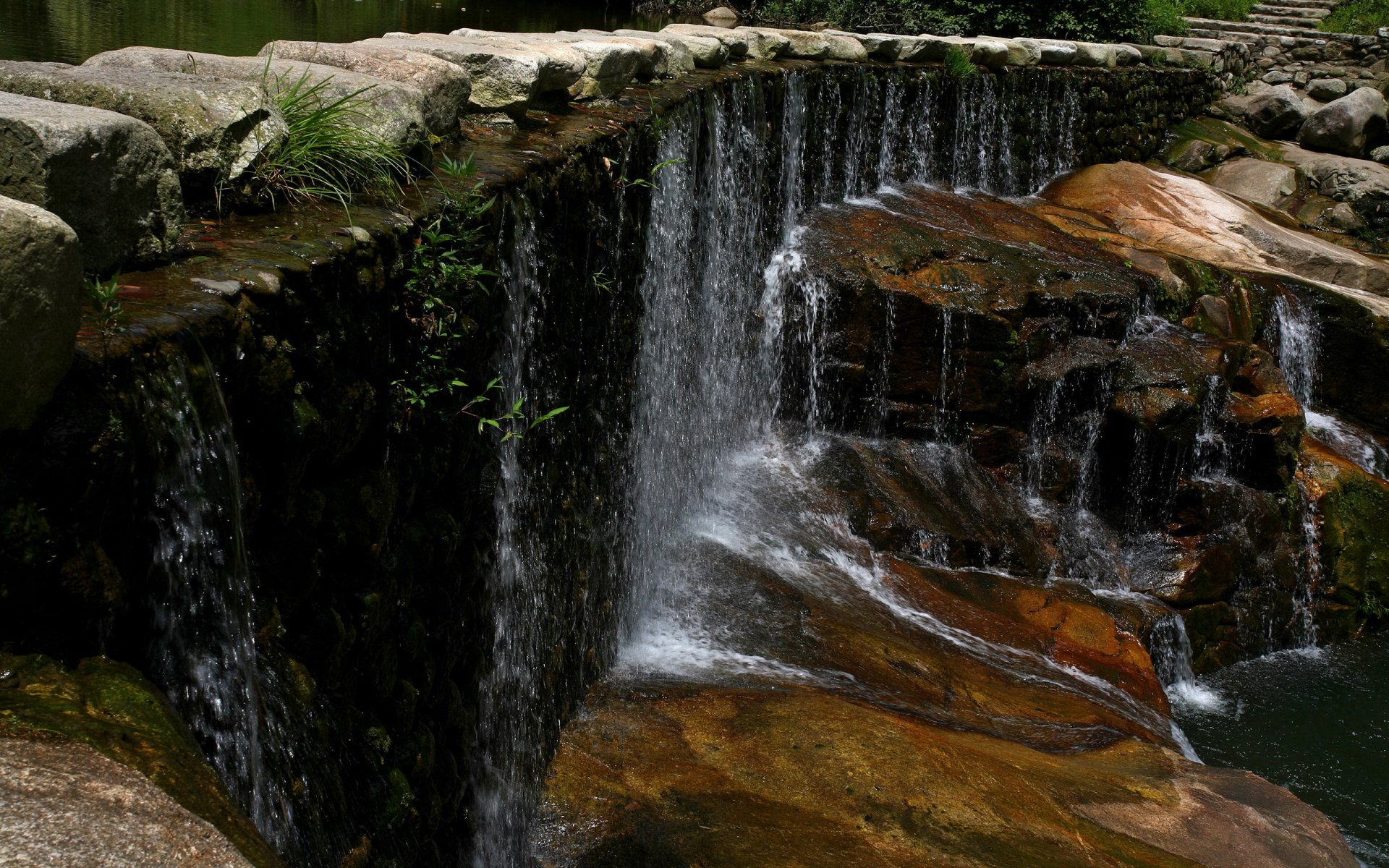 HD photography of a flowing waterfall cascading over rocks, surrounded by greenery, captured as a serene water-themed PC desktop wallpaper.