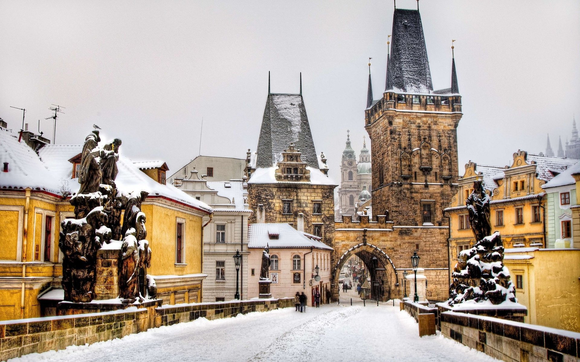 Snowy Prague scene: a man-made stone bridge leading to Gothic castle towers, presented as a 2K Quad HD PC desktop wallpaper background.