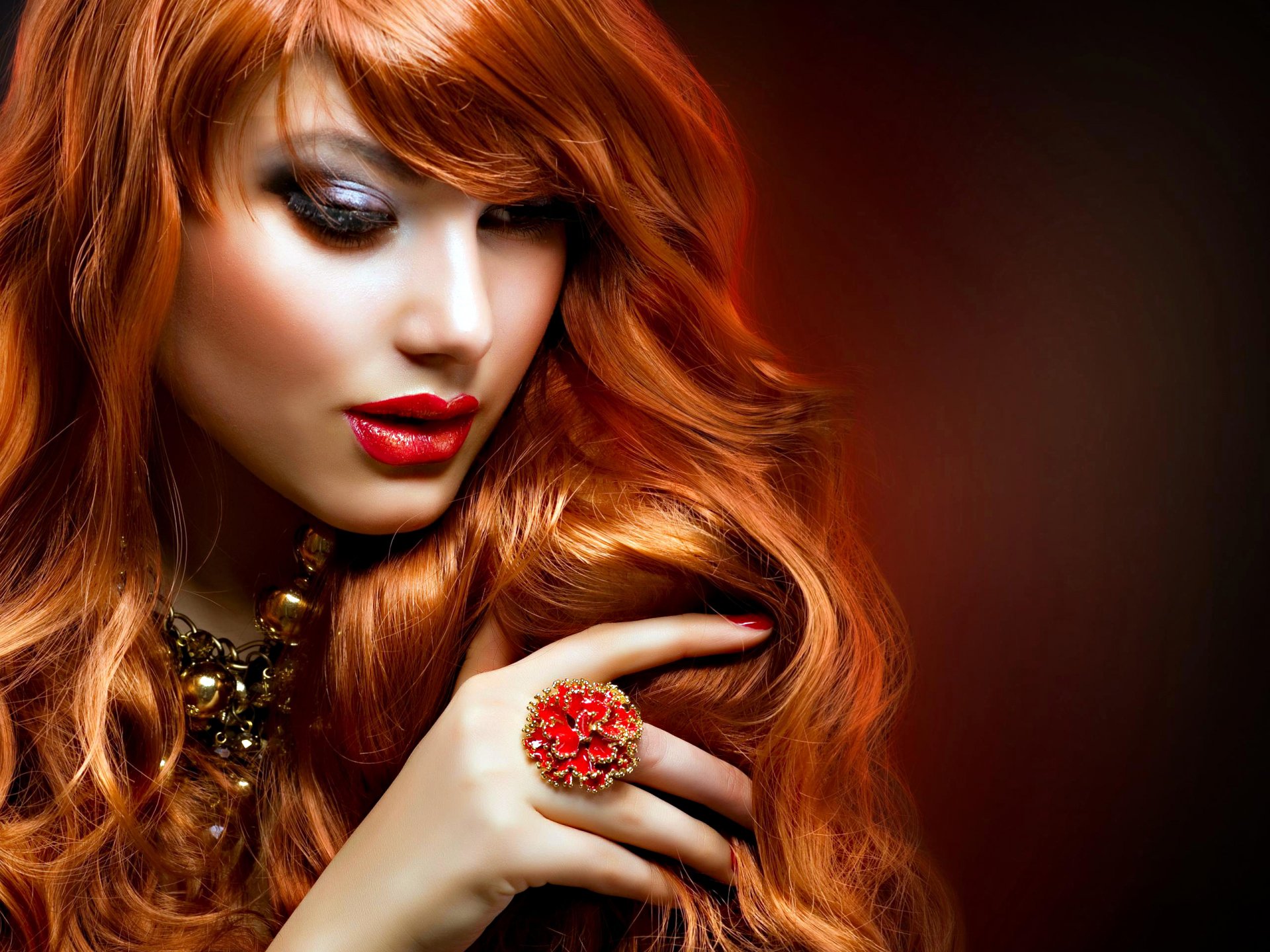A woman with stunning red hair and bold makeup gazes thoughtfully, wearing a statement ring. This captivating image serves as an HD desktop wallpaper and background.