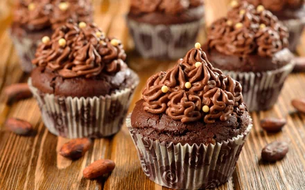 HD desktop wallpaper featuring rich chocolate cupcakes with chocolate frosting and golden sprinkles on a rustic wooden surface.
